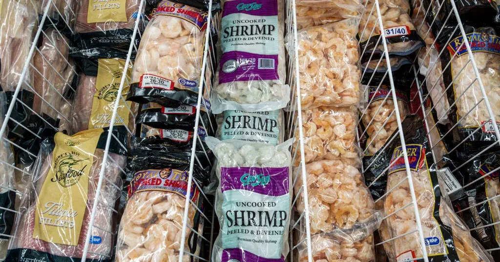 Frozen shrimp and seafood packages stacked on wire freezer shelves in a store.