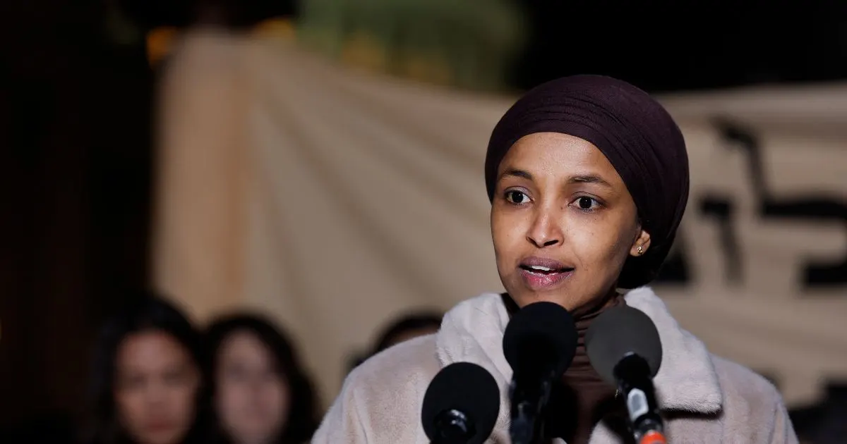 A woman in a brown head covering speaks at microphones at a nighttime outdoor event.