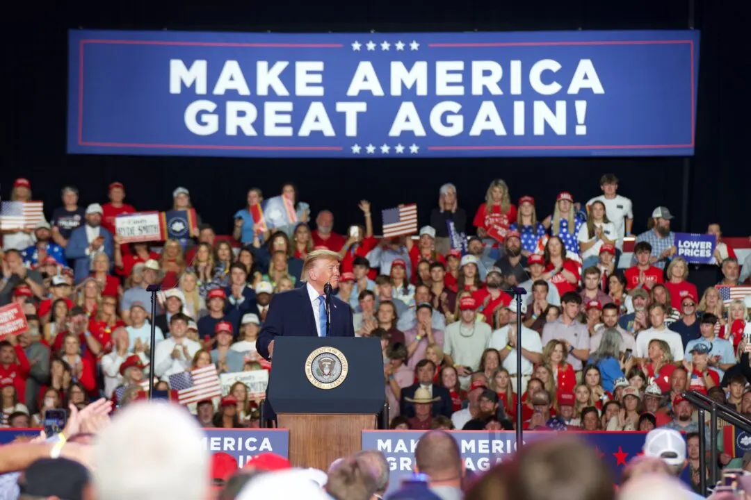 Speaker at a podium before a crowd under a Make America Great Again banner, with American flags.