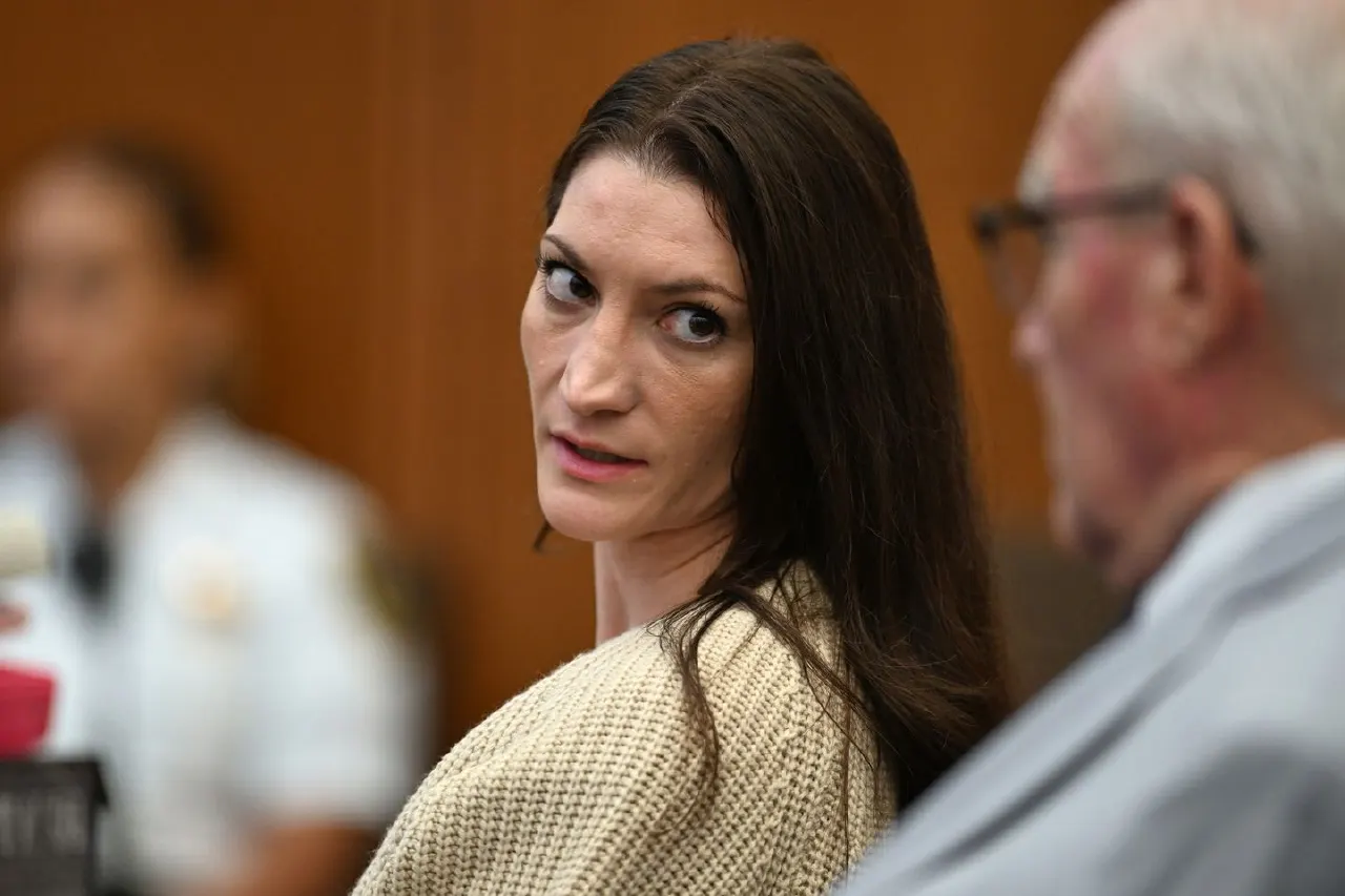Woman with long dark hair glances back over shoulder beside an older man in a courtroom.
