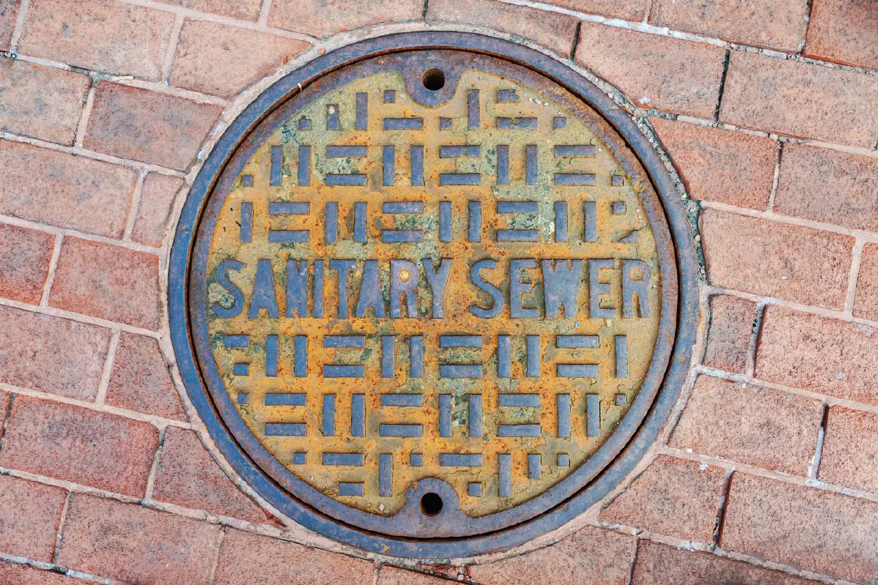 Round cast-iron manhole cover reading SANITARY SEWER set in red brick pavement.