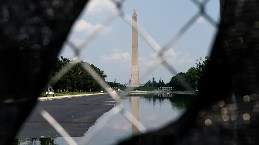 Washington Monument seen through chain-link fence across the reflecting pool on the National Mall.