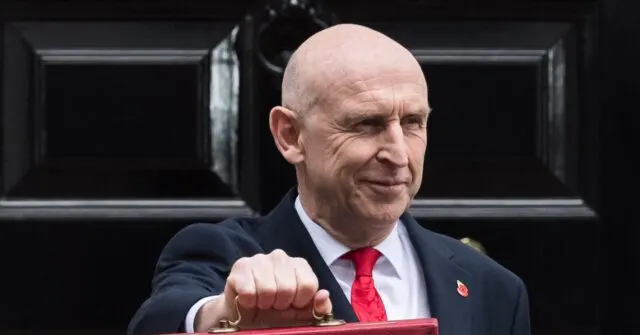 Bald man in dark suit and red tie holding a red budget box outside a black door.