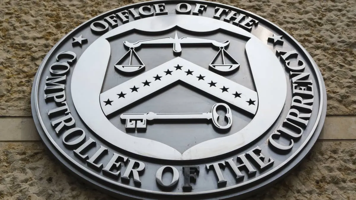 Metal Office of the Comptroller of the Currency seal mounted on a stone building wall.