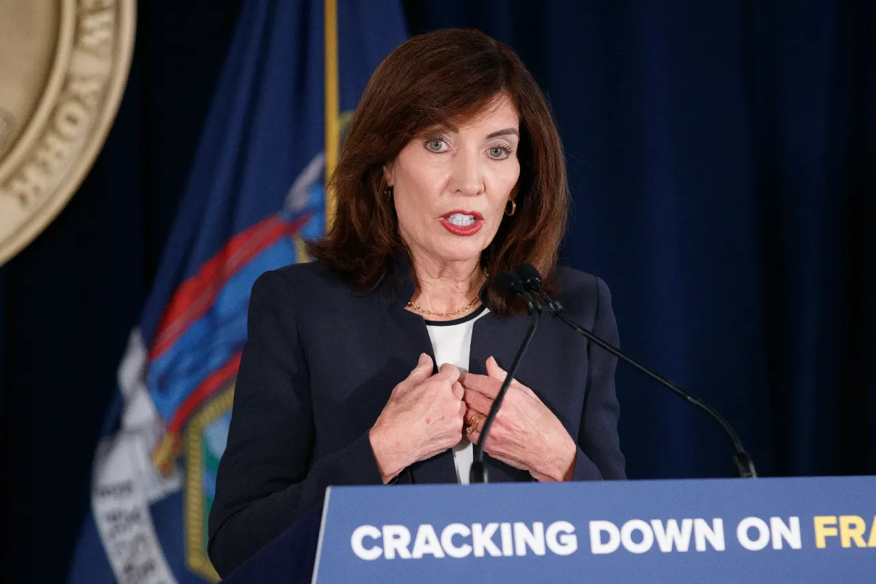 Woman in dark blazer speaking at podium with blue banner reading Cracking Down On Fraud