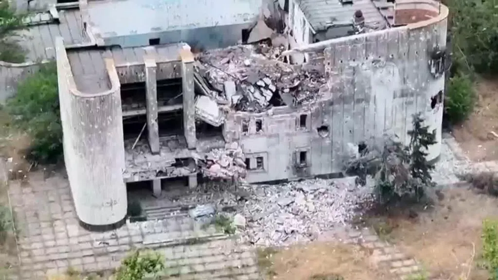 Aerial view of a heavily damaged concrete building with collapsed roof and rubble.