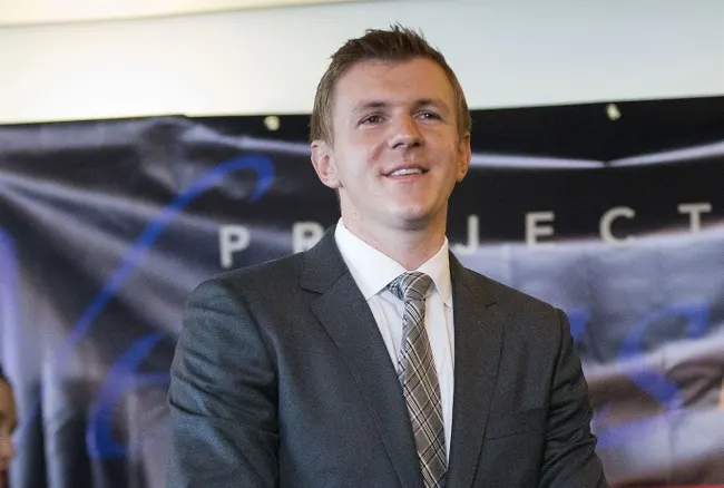 Smiling man in dark suit and tie in front of a partial banner reading "PROJECT"