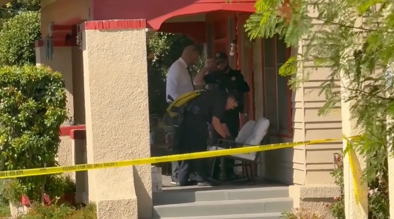 Police tape across a house porch where officers and a seated person stand near a chair.