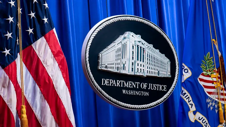 Department of Justice seal on blue curtain beside American flag and DOJ flag