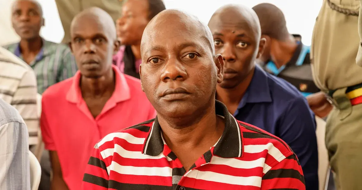 Group of men standing in a crowded room, one man in striped polo facing camera, uniformed person at right edge.