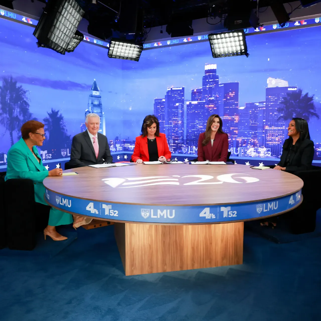 Five people seated at a round debate table on a TV studio set with LA skyline backdrop.