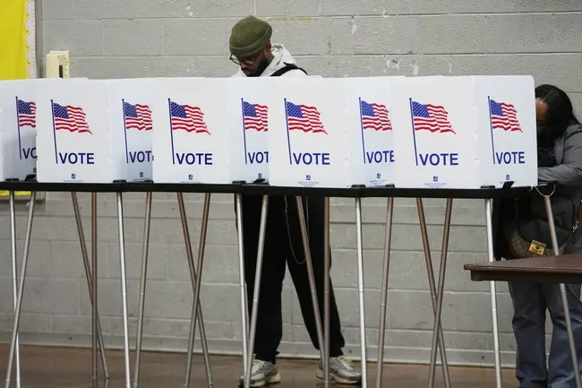 Voters at polling booths decorated with American flags and VOTE signs in a gymnasium.