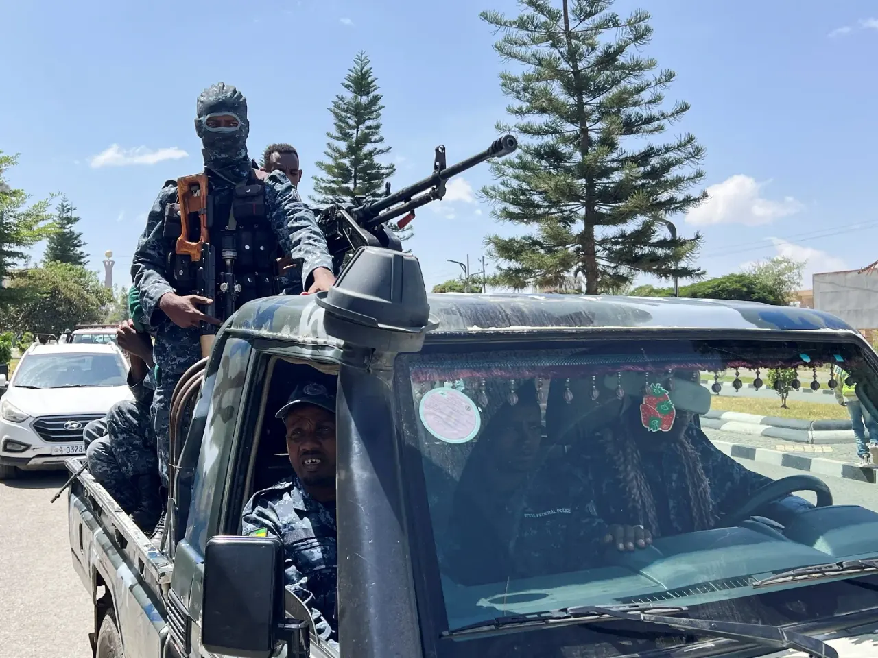 Armed uniformed men with rifles and a mounted machine gun ride in a pickup truck on a city street.