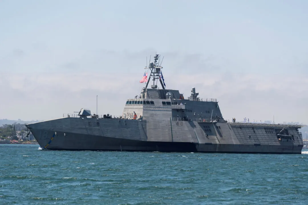Grey littoral combat ship with US flag sailing on open water under hazy sky