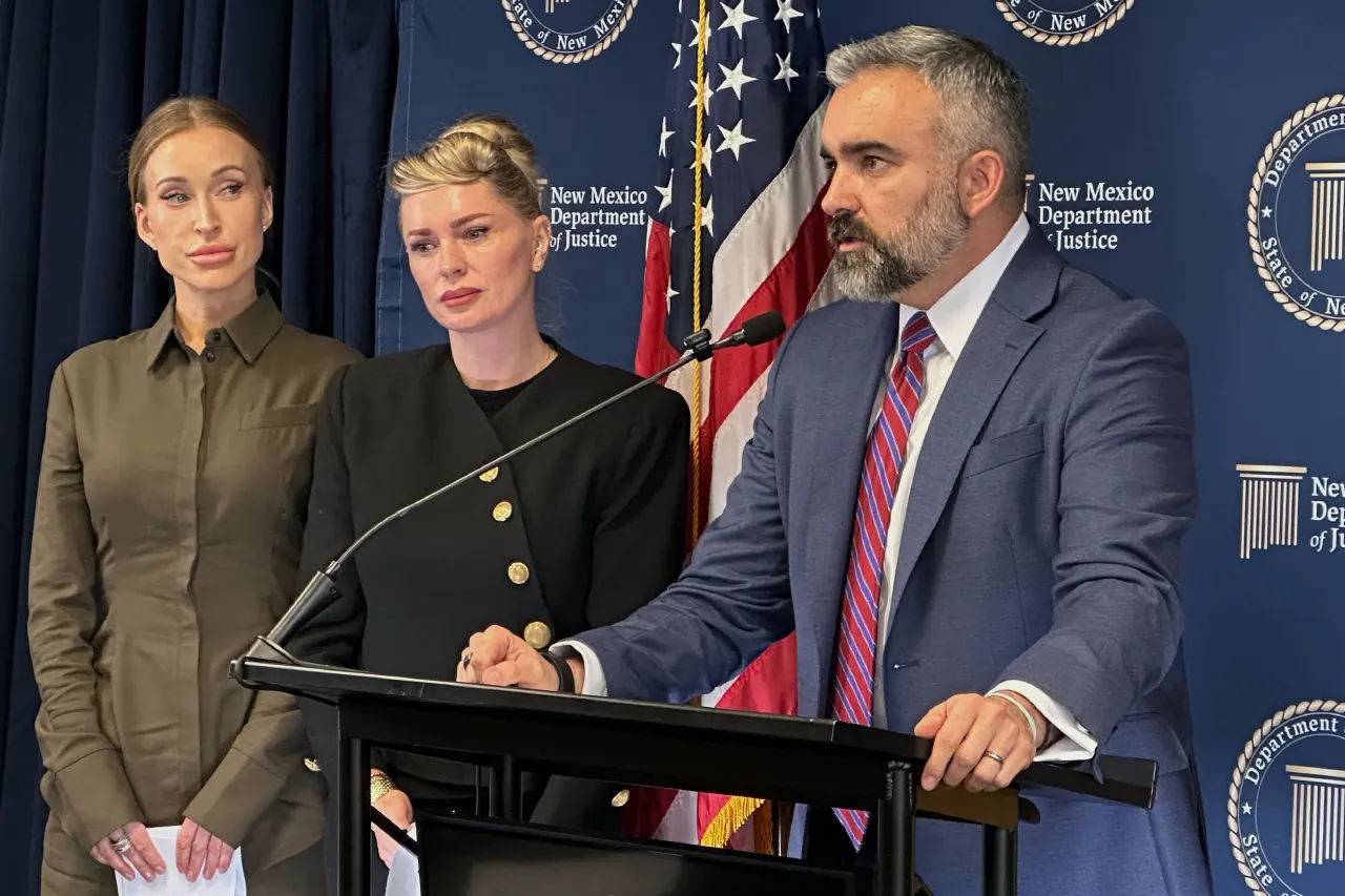 Three people at a podium before New Mexico Department of Justice backdrop and American flag.