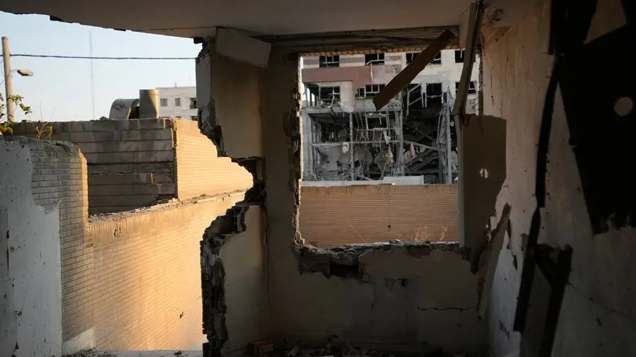 Damaged building interior with shattered walls and exposed rubble, viewed through a blown-out opening.
