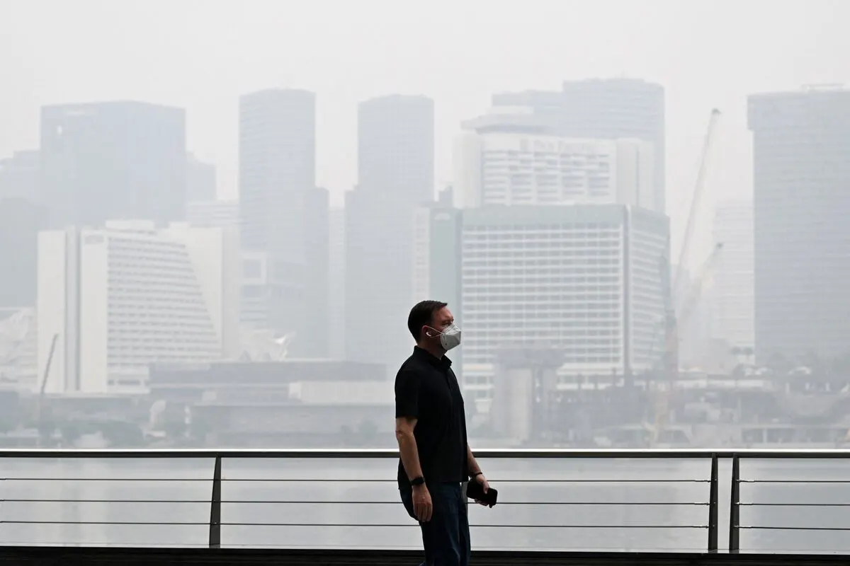 Masked man on waterfront walkway, city skyline shrouded in thick haze.