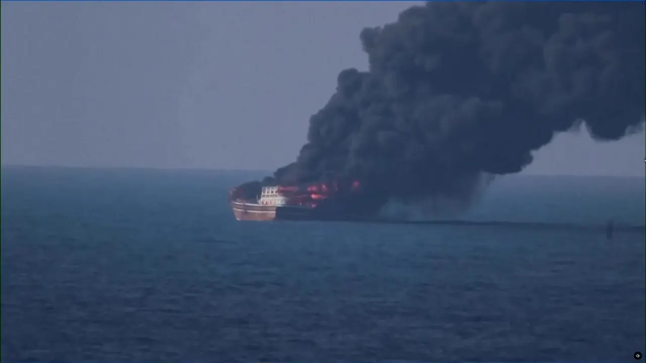 A wooden dhow burning at sea, releasing thick black smoke over calm water.