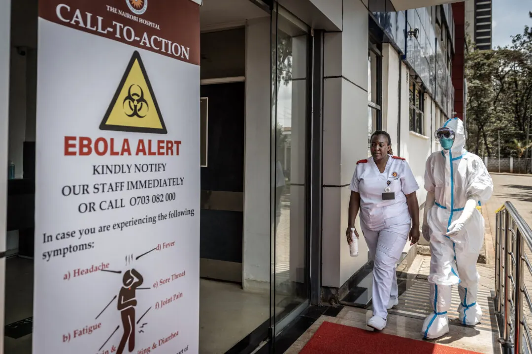 Nurse and worker in protective suit beside Ebola alert sign at Nairobi hospital entrance.