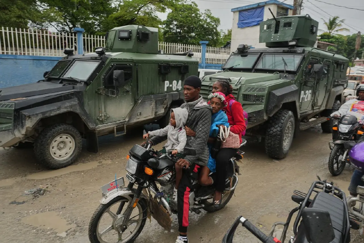 Family riding a motorbike past two armored military vehicles marked P-84 on a muddy street.