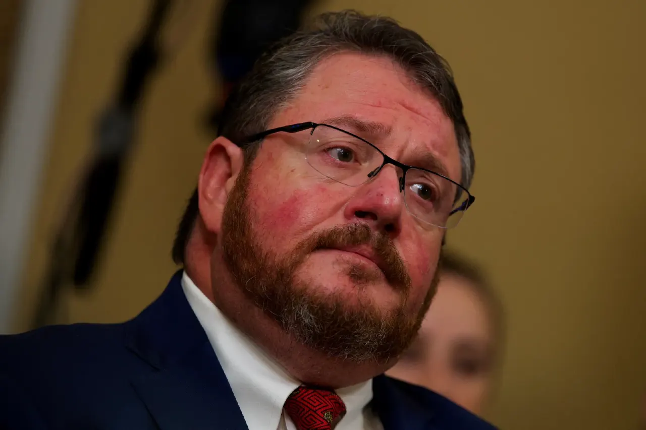 Bearded man in glasses and navy suit looking sideways, close-up, indoors.