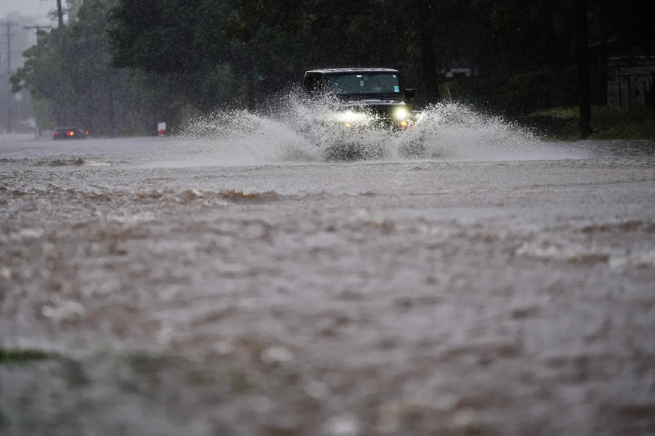 Vehicle plowing through floodwater on a rain-soaked road during a heavy storm.