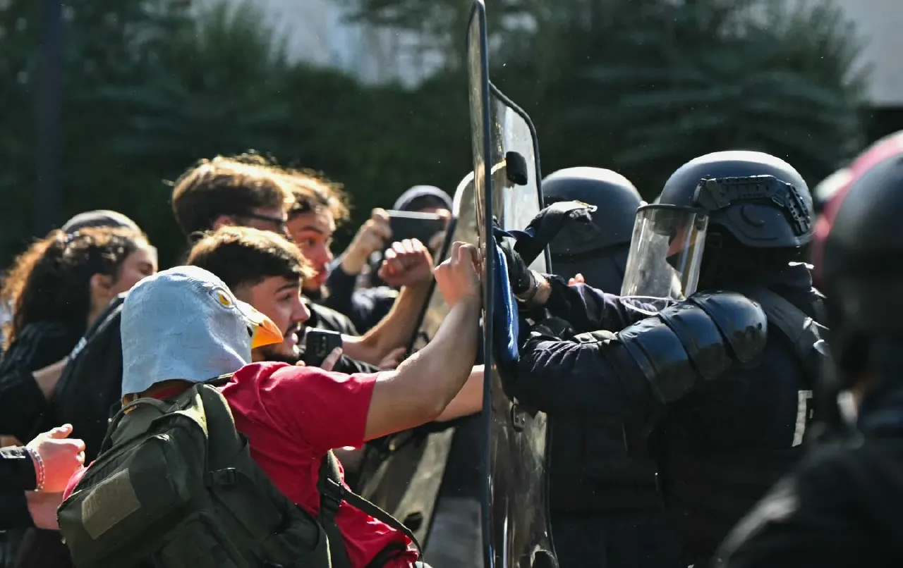 Young protesters pushing against riot police in helmets and shields during a confrontation
