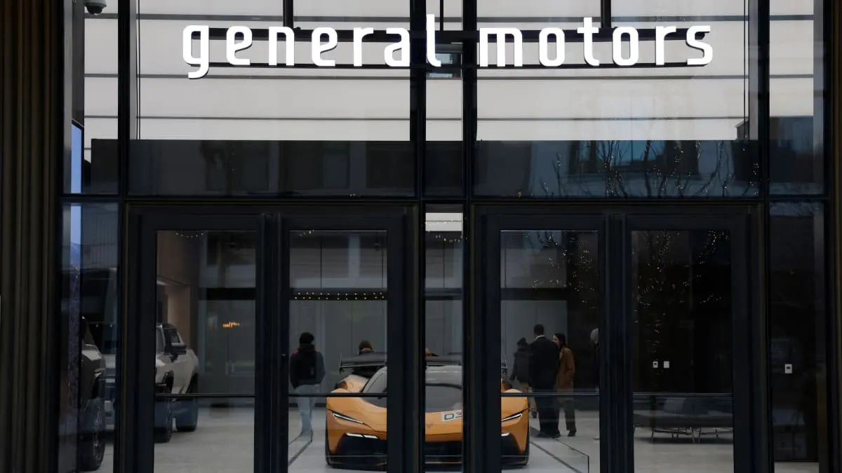 General Motors building entrance with lit sign and orange concept car visible through glass doors.