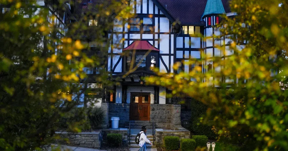 Tudor-style campus building framed by autumn leaves, with a lone student walking up the steps.