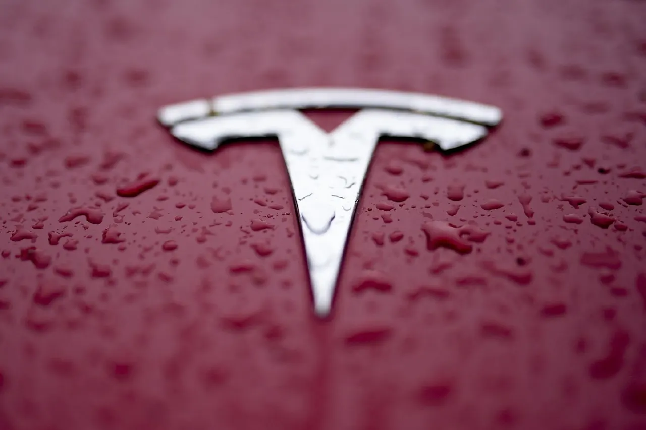 Close-up of Tesla logo on a rain-beaded red car hood.