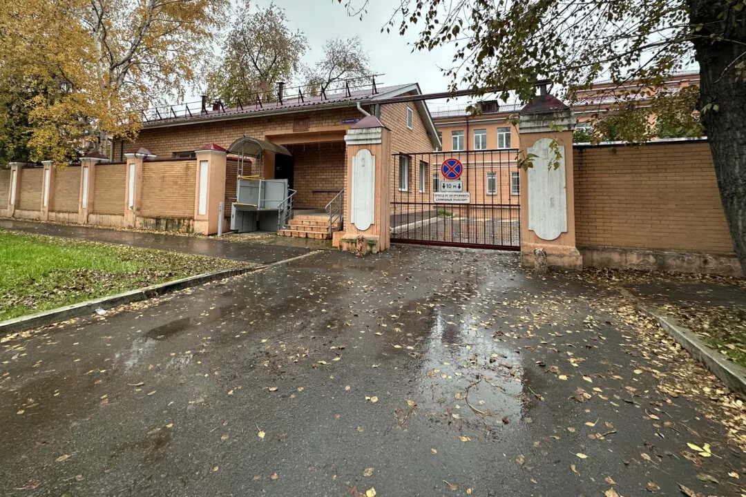Brick building with gate and no-parking sign visible, autumn setting with wet pavement.