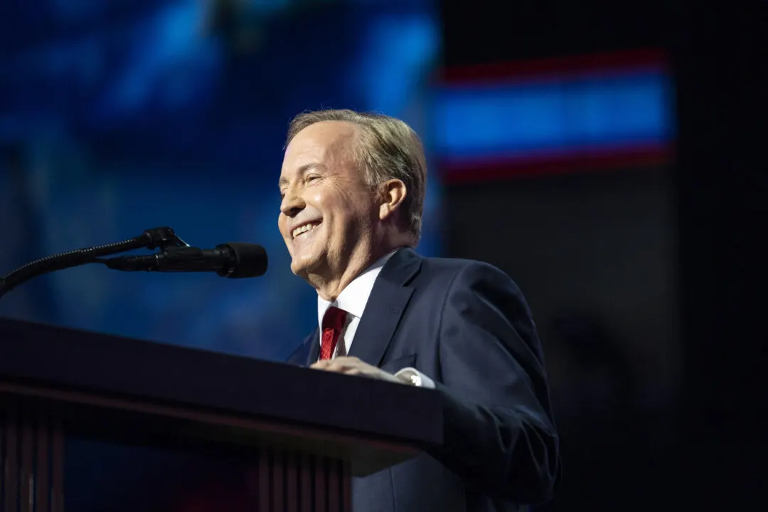 Smiling man in dark suit and red tie speaking at a podium with microphone
