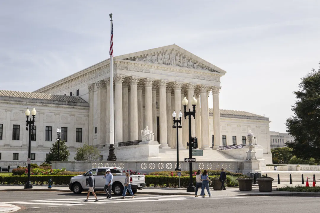 The white marble Supreme Court building with columns and pediment, with pedestrians and a white pickup on the street.