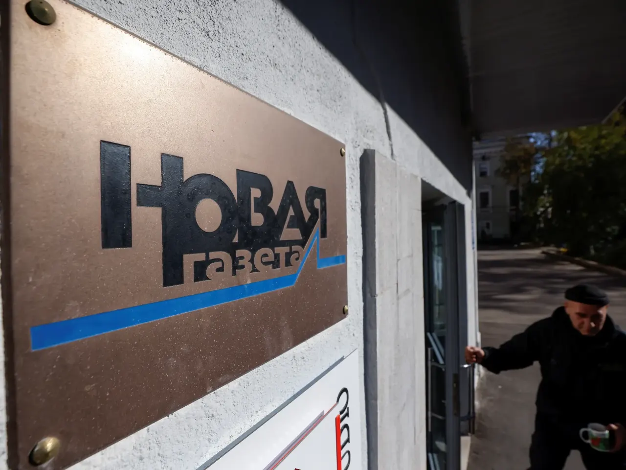 Novaya Gazeta sign on building wall, with a man in a cap walking past