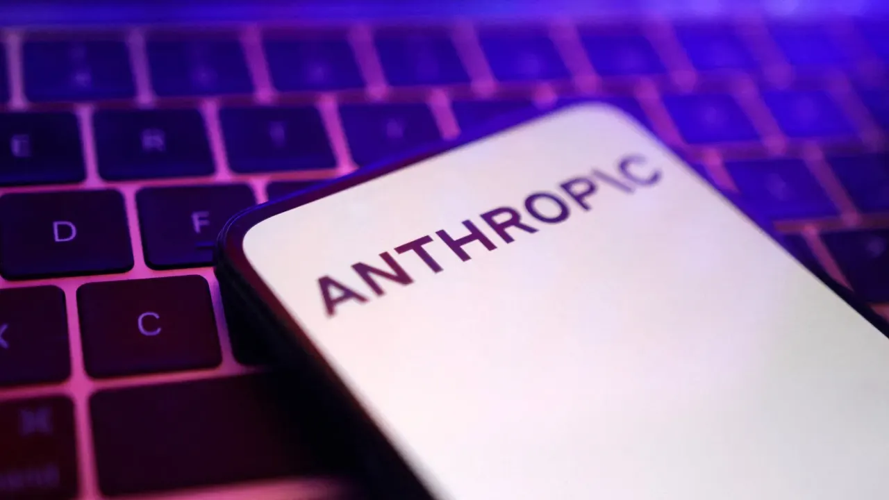 Smartphone screen displaying the Anthropic wordmark resting on a glowing purple illuminated keyboard.