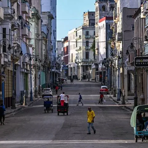 Nearly empty street in Havana with pedestrians, bicycle taxis and colonial-era buildings.