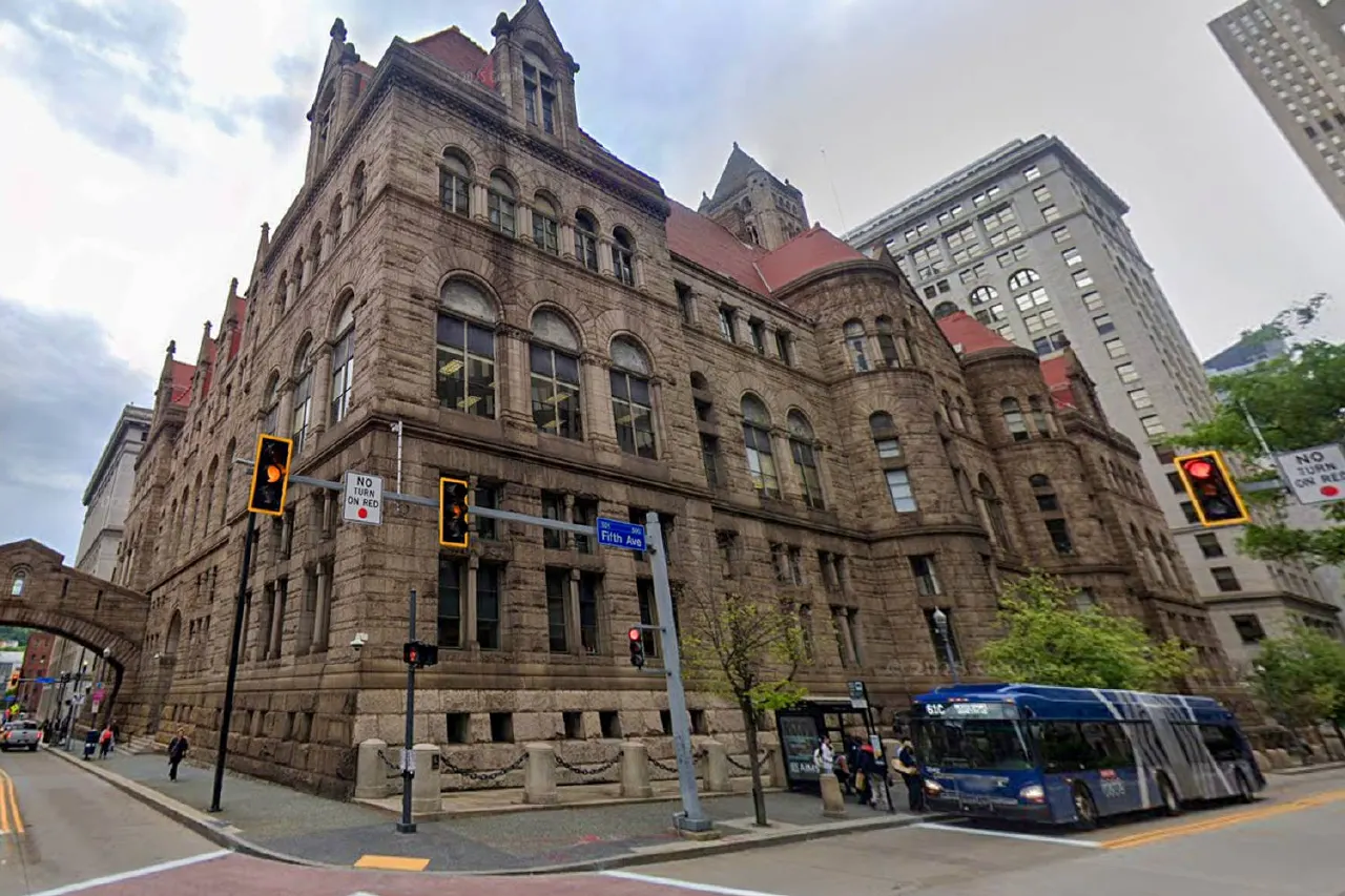 Large historic stone courthouse-style building on a Pittsburgh street corner, with a passing bus.