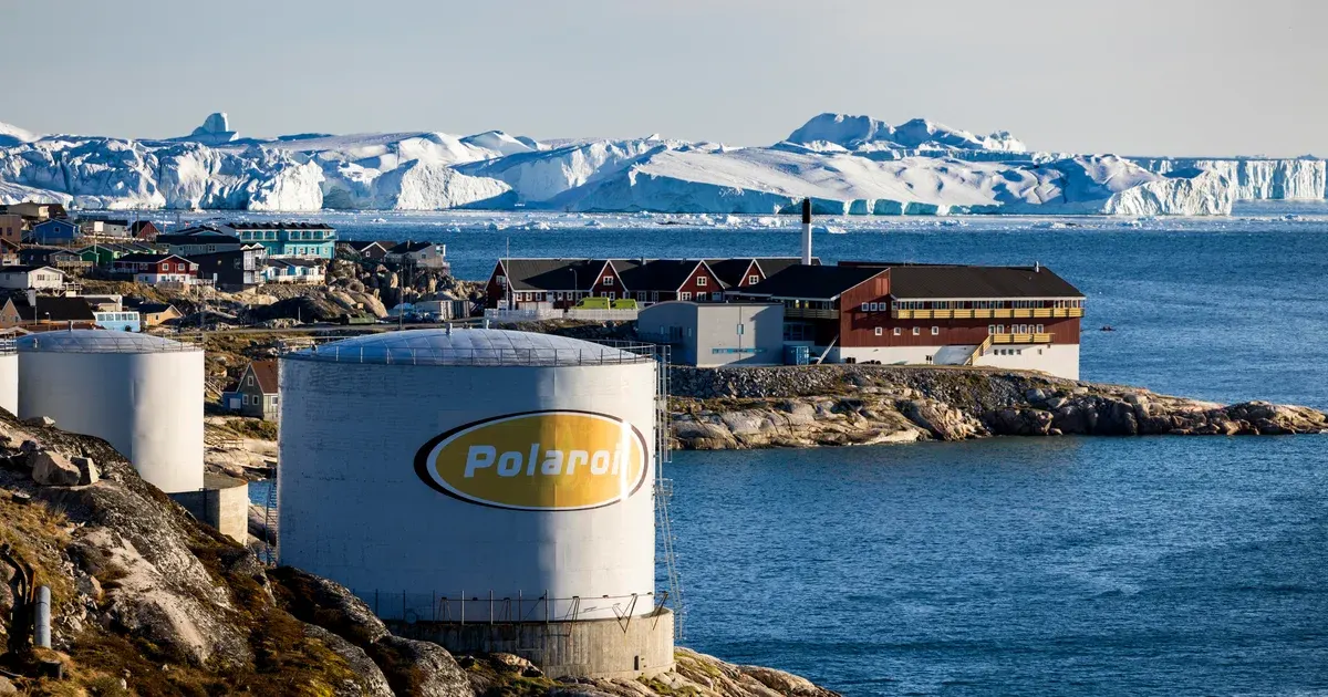 Coastal Greenland town with fuel storage tanks bearing Polaroil logo, icebergs behind.