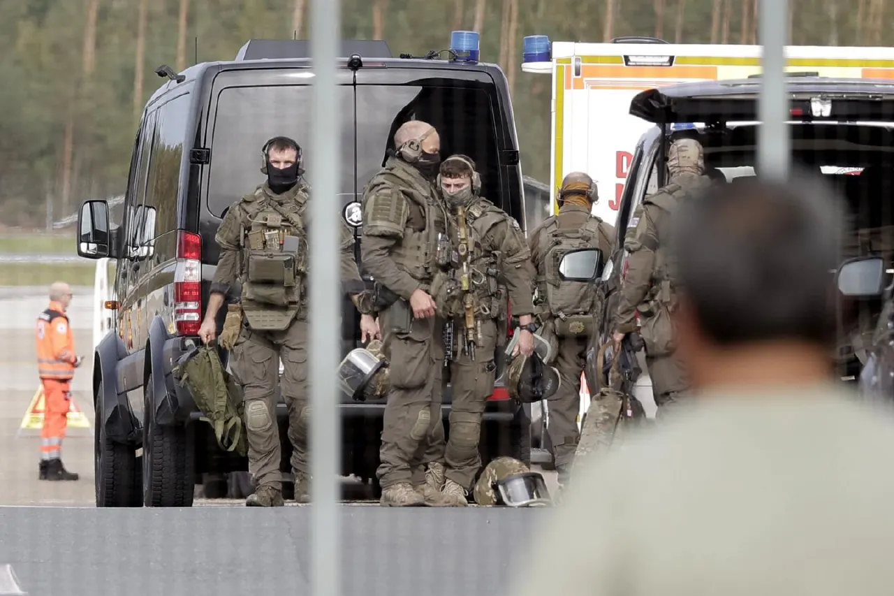 Armed tactical officers in dark gear beside a police van and ambulance on an airport apron.