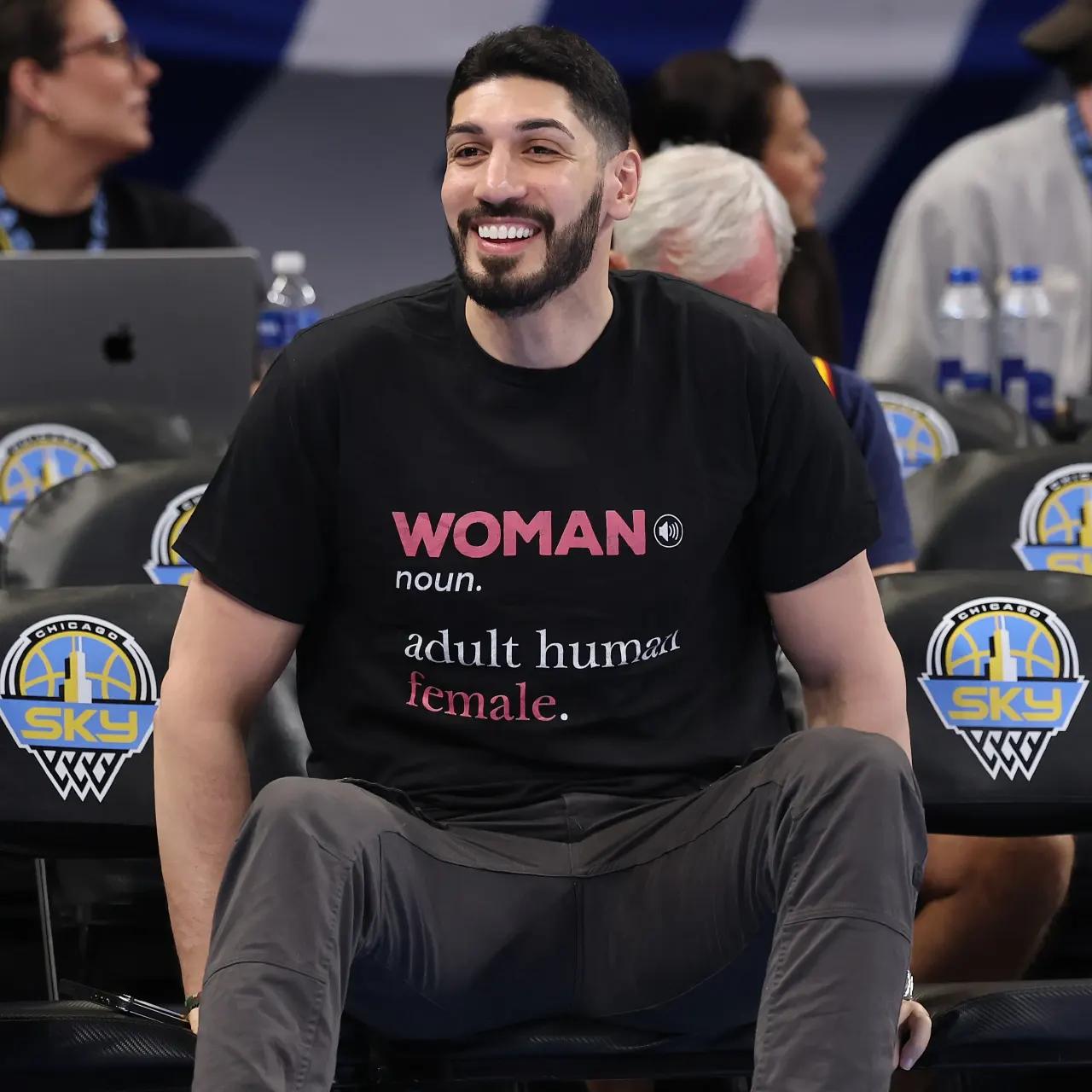 Smiling bearded man in black slogan T-shirt seated courtside at a Chicago Sky game.