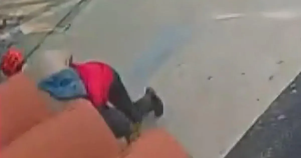Blurry surveillance footage of a person in red and black on a gas station pavement, foreground blurred