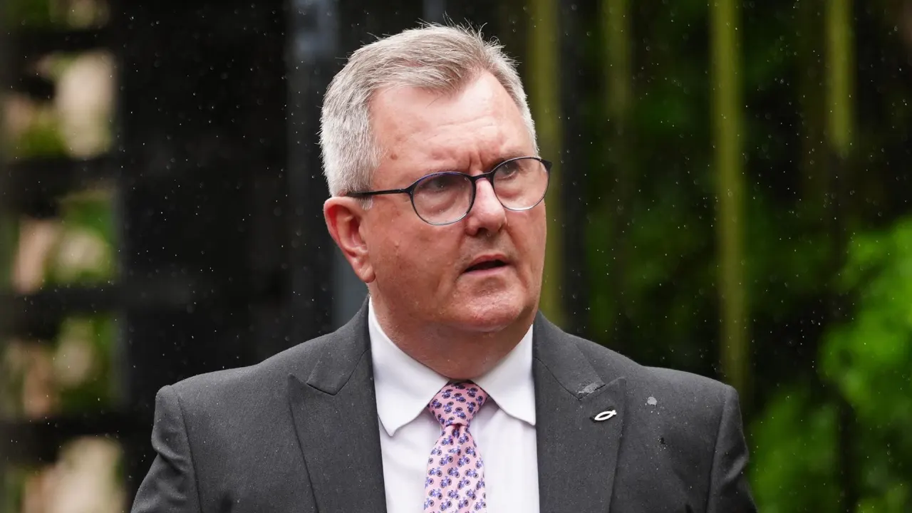 Older man with grey hair and glasses in dark suit and patterned tie, outdoors in rain.