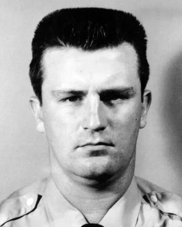 Black-and-white studio portrait of a man with short dark hair in a collared shirt.