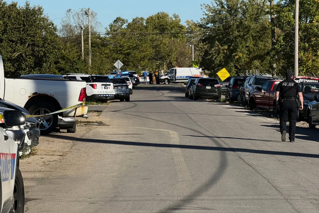 Police cruisers, tape and officers on a residential street, with parked cars and vehicles.