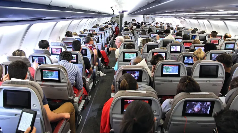 Passengers seated in rows inside an airplane cabin, with seatback screens on.