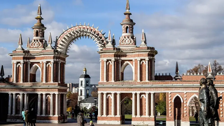 Ornate red brick gateway with spires and statues at Tsaritsyno park, with a few visitors.