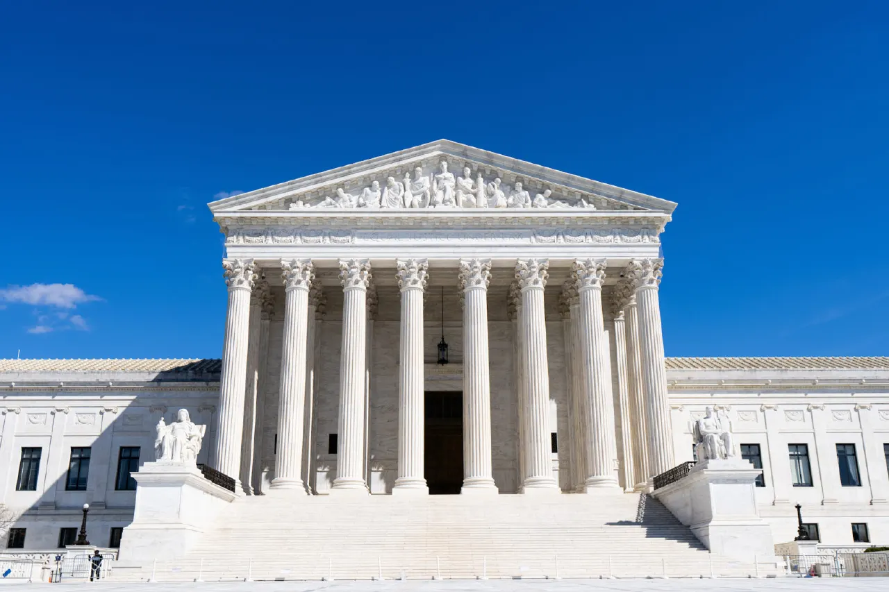 White marble Supreme Court building facade with columns, pediment sculpture, and blue sky.