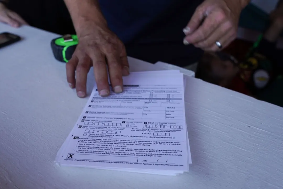 Hands with a ring pressing down on stacked voter registration forms on a white table.