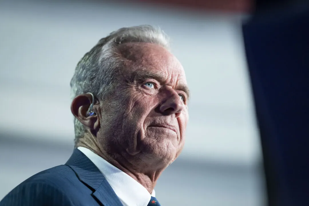 Older man with gray hair, earpiece and navy suit, looking off-camera at an event.