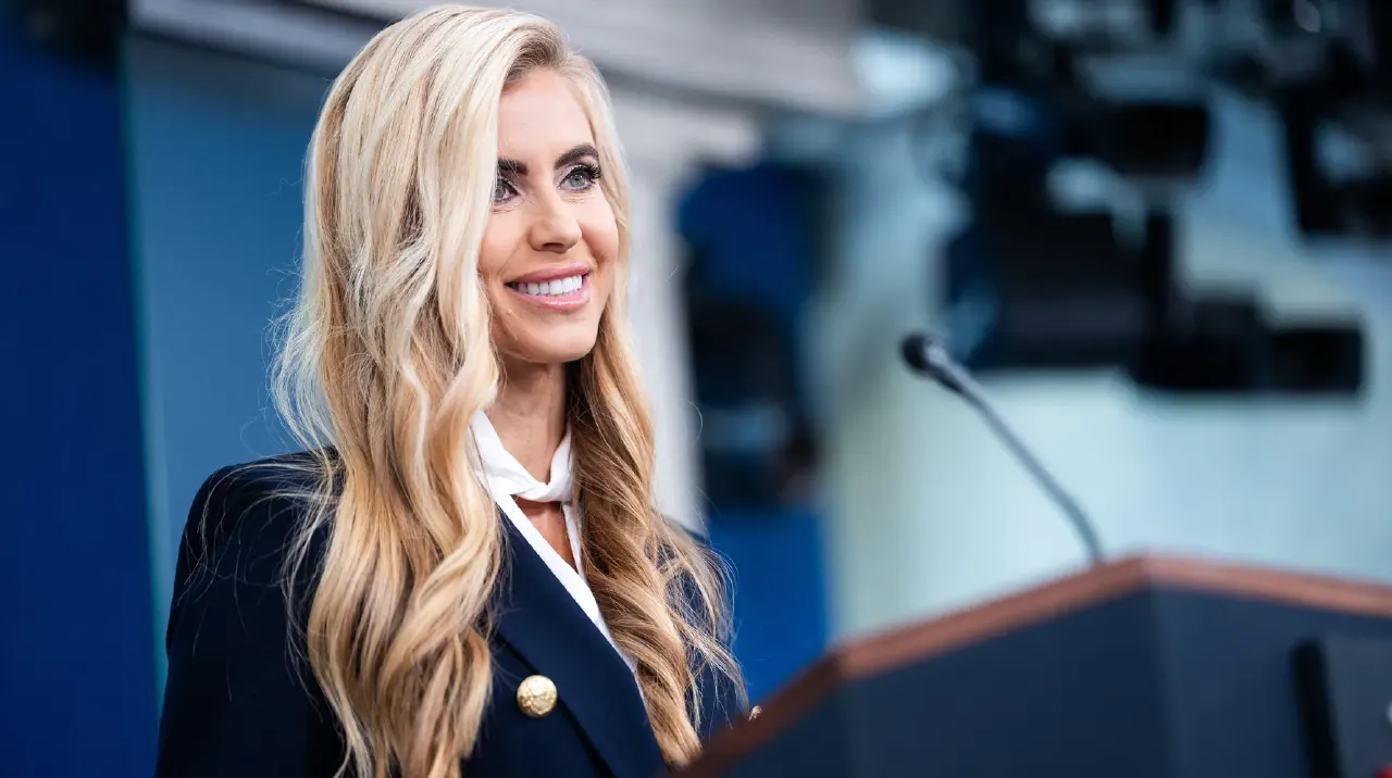 Smiling woman with long blonde hair at a podium in a press briefing room